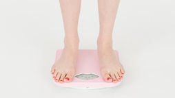 Feet with red nail polish stand on a pink scale on a white background, suggesting a setting focused on weight measurement.