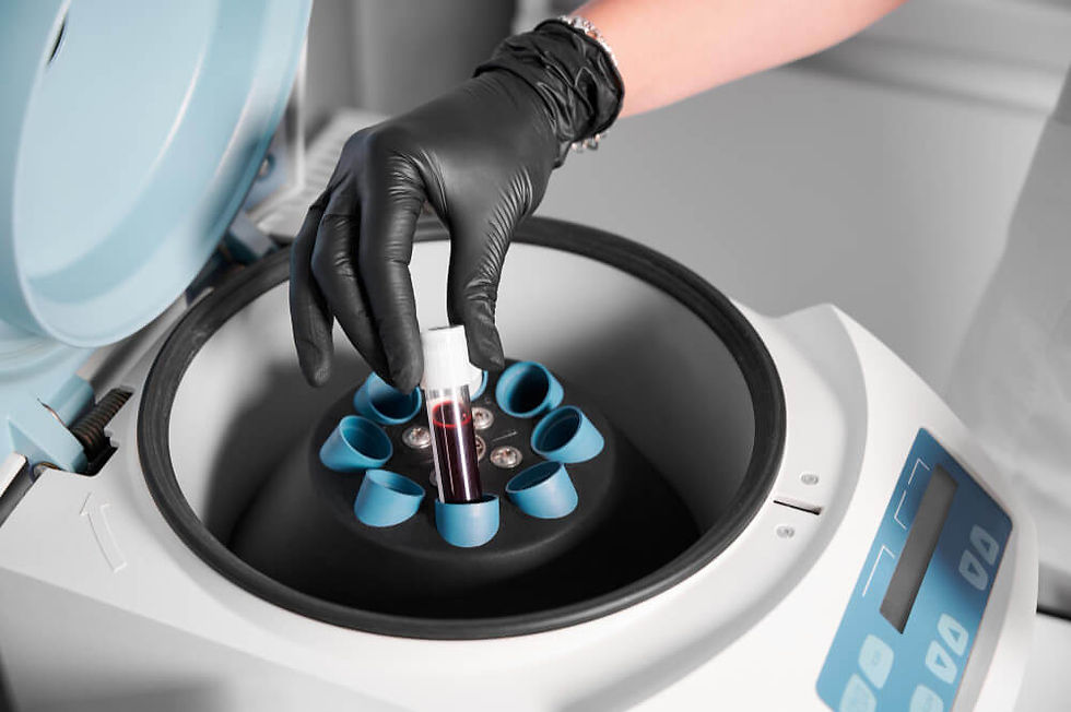 Gloved hand places a blood sample tube into a centrifuge in a lab, with a blue digital control panel.
