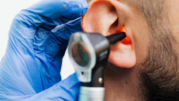 Gloved healthcare professional examines a patient’s ear with an otoscope before fitting a hearing aid.