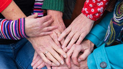 Hands of diverse individuals stacked together, with colorful patterned sleeves, symbolizing unity and support in personalized care.