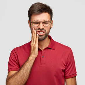 Man in red polo and glasses holds his cheek, eyes shut in pain against a plain gray background.
