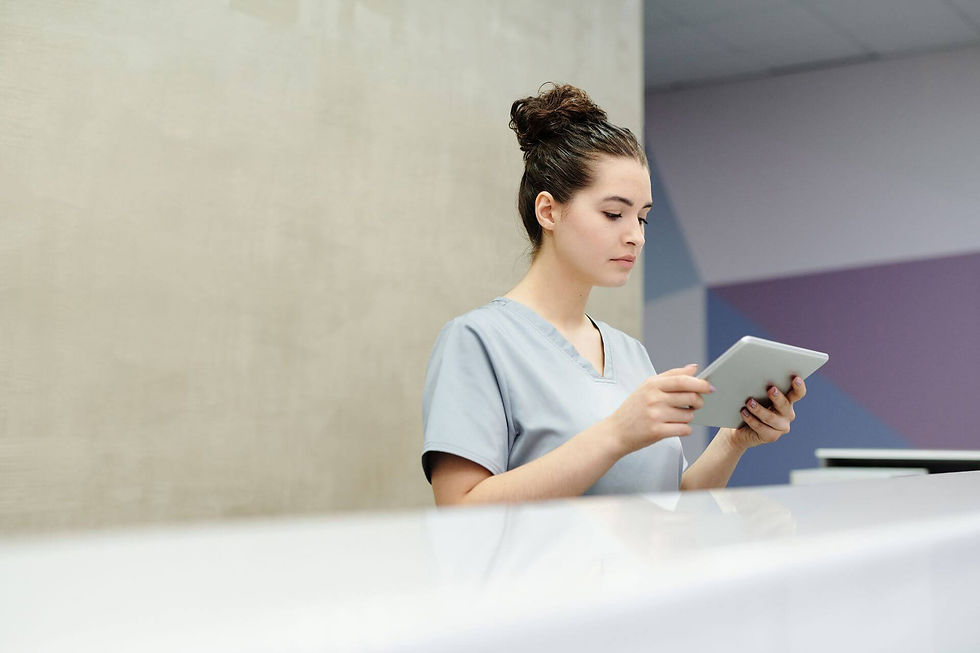 A receptionist in scrubs using a tablet at an office reception desk