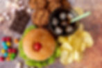 Top view of a plate with a hamburger paired with sweet snacks, showcasing an assortment of unusual food pairings that represent weird pregnancy cravings combinations.