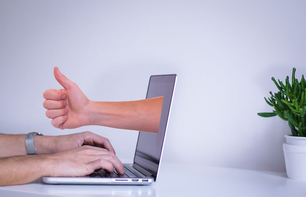 Hands typing on a laptop with a virtual arm on the screen giving a thumbs-up; a small plant sits on a white desk, suggesting a futuristic workspace focused on FDA approval.