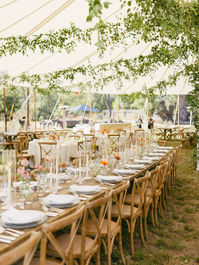 Long wooden banquet table in a family style wedding tent.