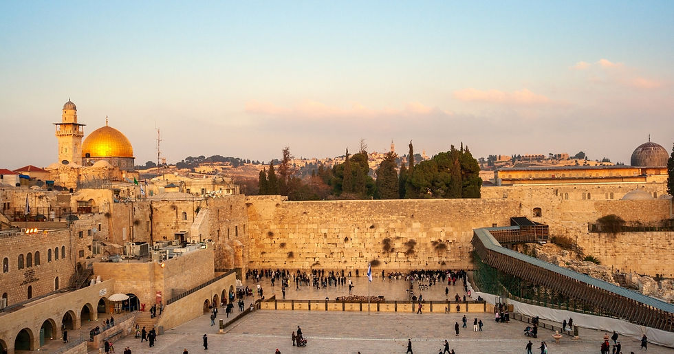 A bustling square with people at the Western Wall, Jerusalem. Golden dome and trees in the background under a blue and pink sky.