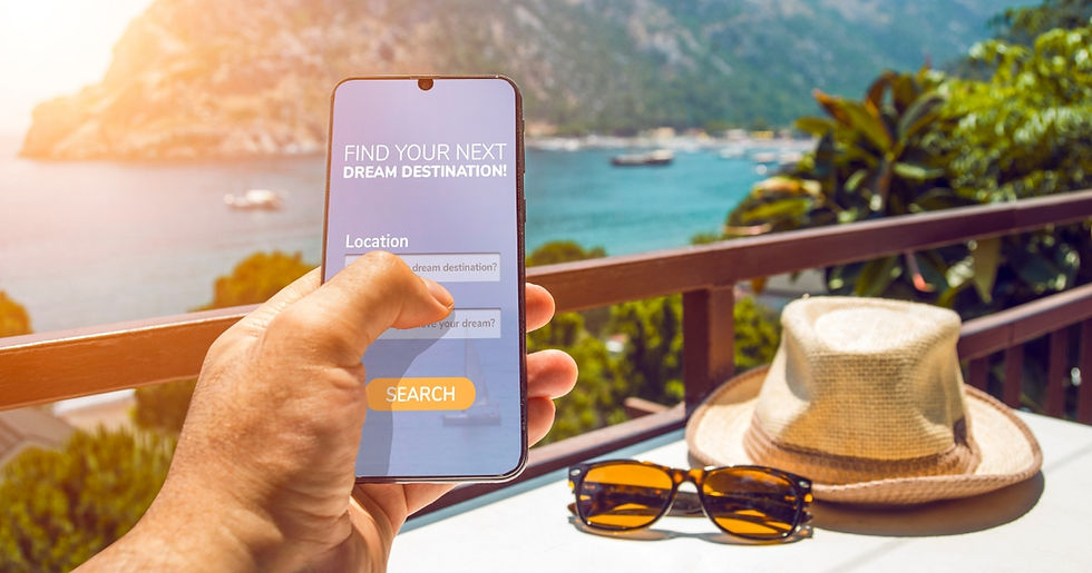 Hand holds phone displaying "Find Your Next Dream Destination" above a sunny ocean view. Hat and sunglasses on table. Relaxed vibe.
