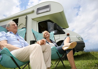Senior couple relaxing in camping folding chairs, camper in background-1