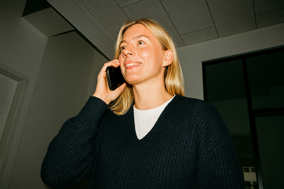 Smiling woman holding a phone, talking, wearing a navy sweater and white shirt.