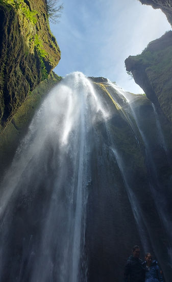 Blick zum Himmel durch eine Öffnung in einer Höhle. Es fällt ein feiner Wasserfall hinein.
