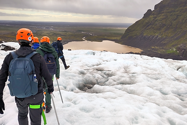 Ein Personengruppe mit Helmen und Stöcken auf dem Eis. Im Hintergrund die Landschaft.