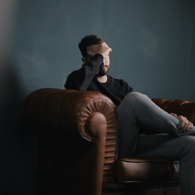 Man sitting on a couch with his head on his forehead, looking sad and overwhelmed.