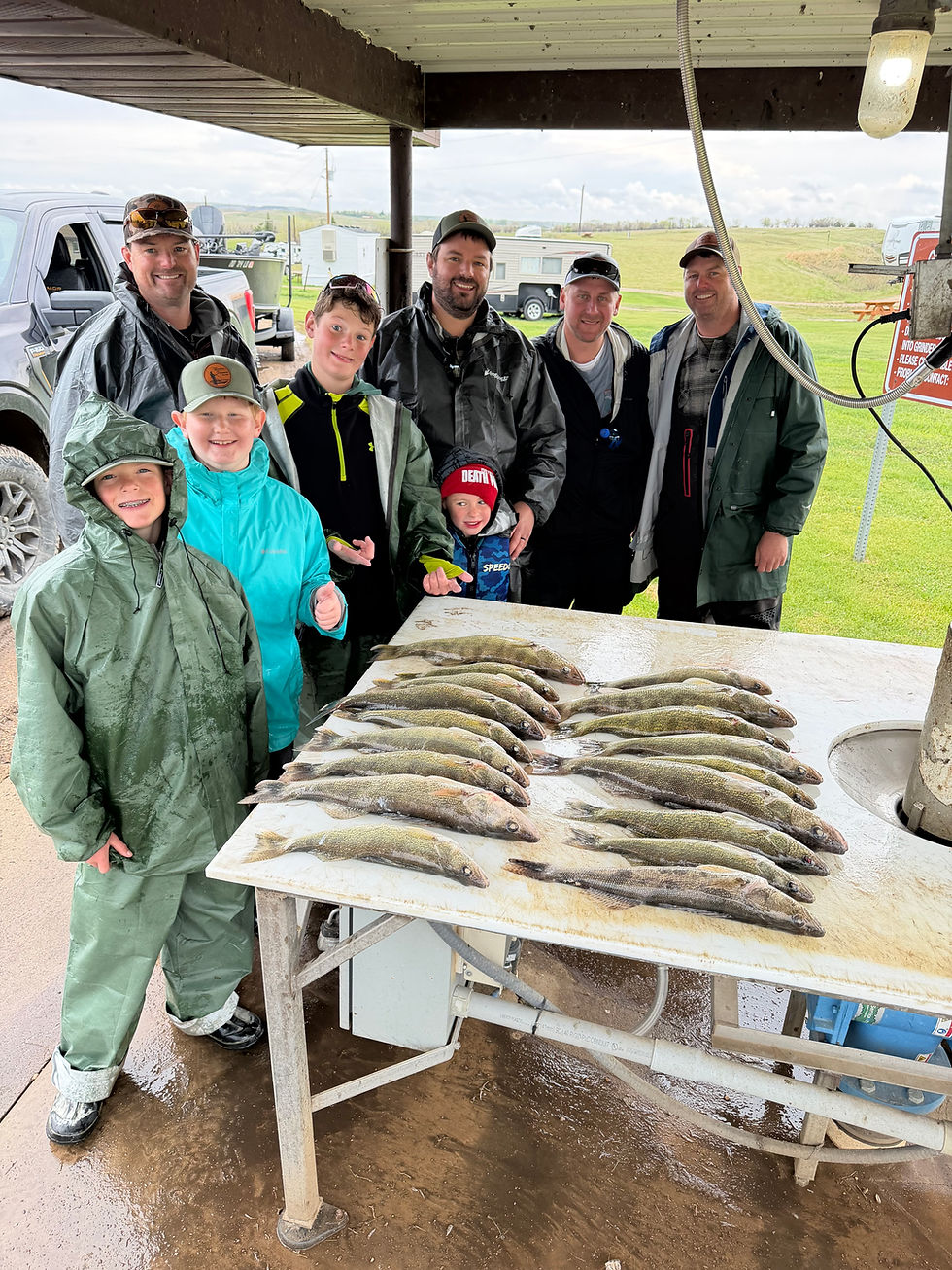 Smiling anglers and kids pose under a fish-cleaning shelter beside a table covered with freshly caught walleye.
