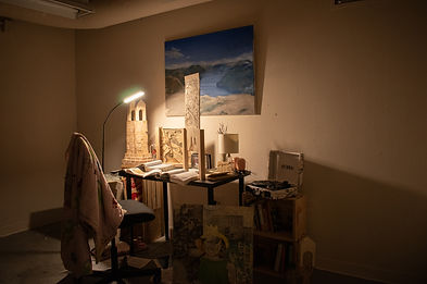 Warm lighting in a dark room that looks like a study far away shot of the desk and chair, there's a painting on the wall