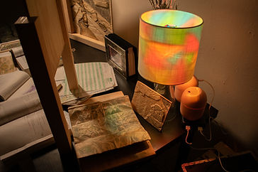 Warm lighting in a dark room that looks like a study with a view of what's on the desk, maps, books, plywood carvings