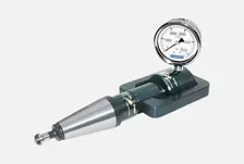 "Hardness tester with an analog dial gauge on a flat base, used for measuring material hardness in industrial and laboratory settings. The device features a cylindrical metal probe and a clearly marked dial for precise readings."