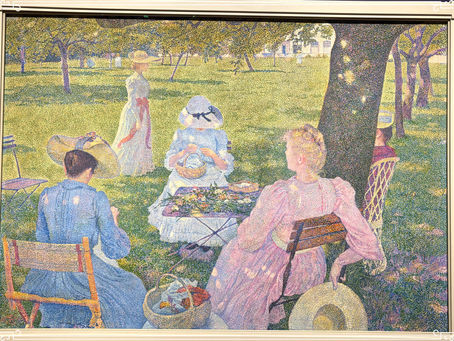 A group of women in vintage attire enjoying a picnic in a sunlit park. A woman knits, others relax. Trees and grass create a serene backdrop.