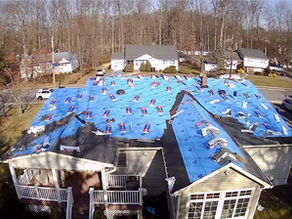 Aerial view of a residential home roof undergoing replacement with blue underlayment and roofing materials installed.