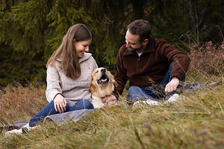 Frauchen und Herrchen mit Golden Retriever sitzen auf einer Decke im Herbstwald
