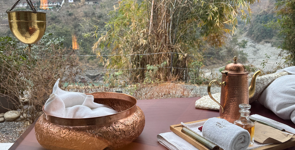 Ayurvedic treatment table with copper pot, warm towels, and oil, overlooking a lush Himalayan valley.