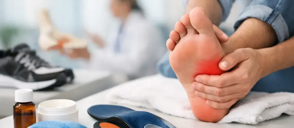 Gloved clinician uses a handheld device with blue light on a patient’s heel in a clinic, suggesting painless foot therapy