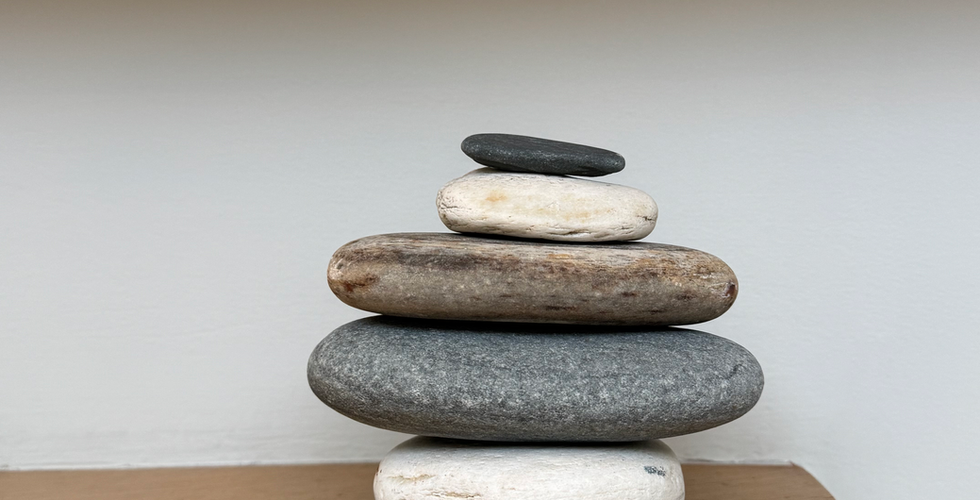 Stacked smooth stones on a wooden shelf, evoking balance, grounding, and the harmony of mind and body.