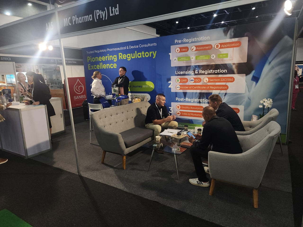 Alternate angle of the Saphex booth showing visitors networking in front of the large regulatory-process graphic wall.
