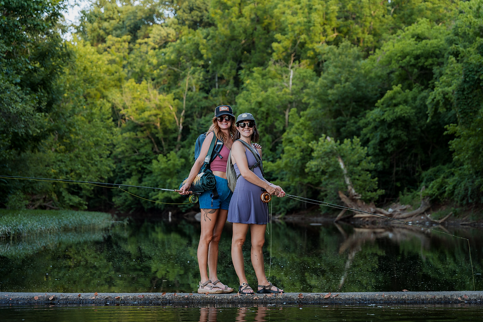 two women fly anglers posing on a rock in the middle of a river.