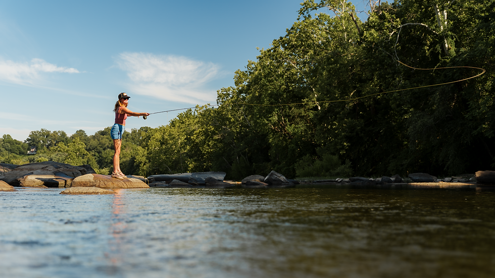 a woman fly fisherman casting a fly rod while standing on a rock next to a river.