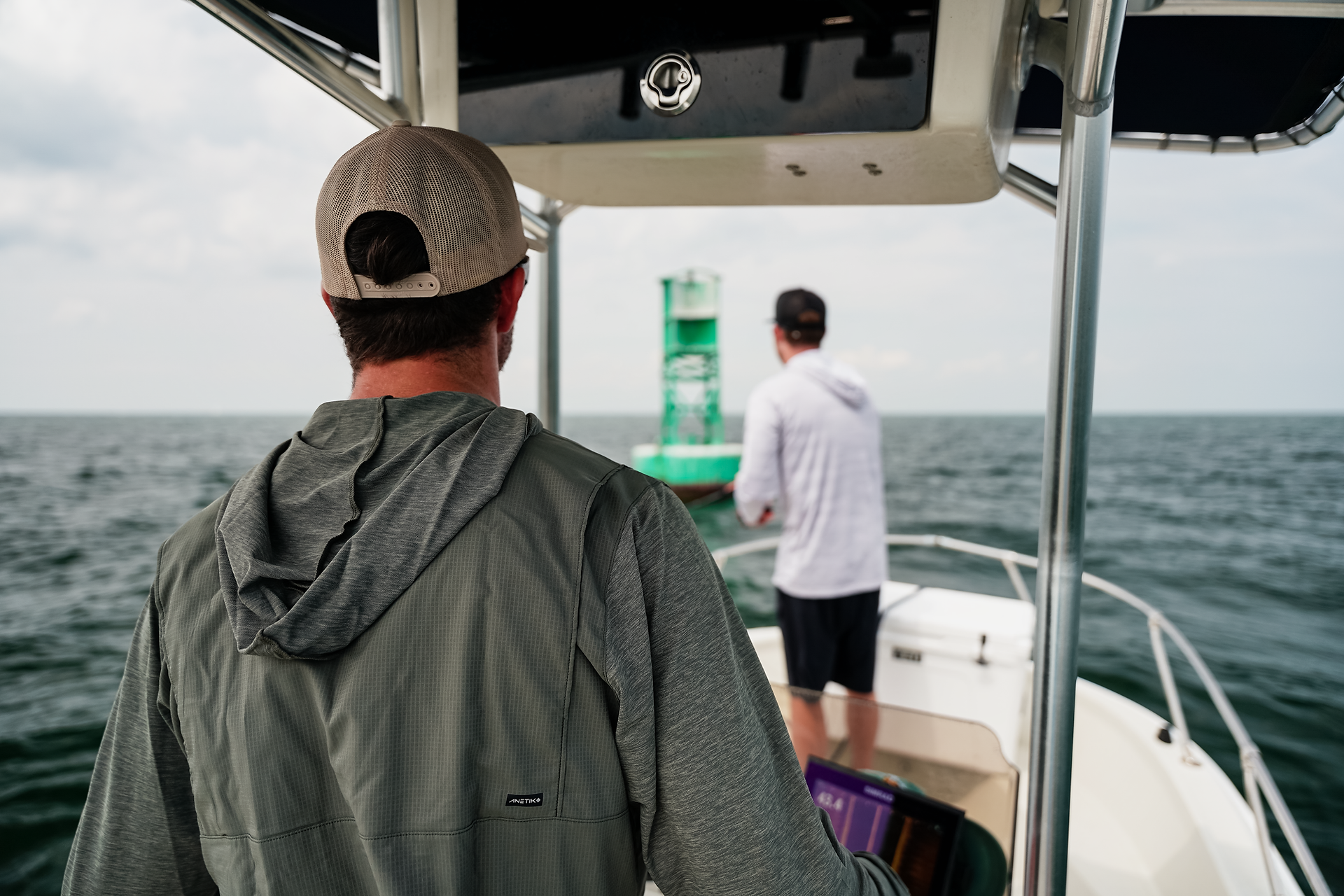 Two fisherman on on a boat casting at a buoy.