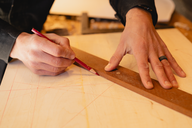 A woodworker marking wood with a pencil.