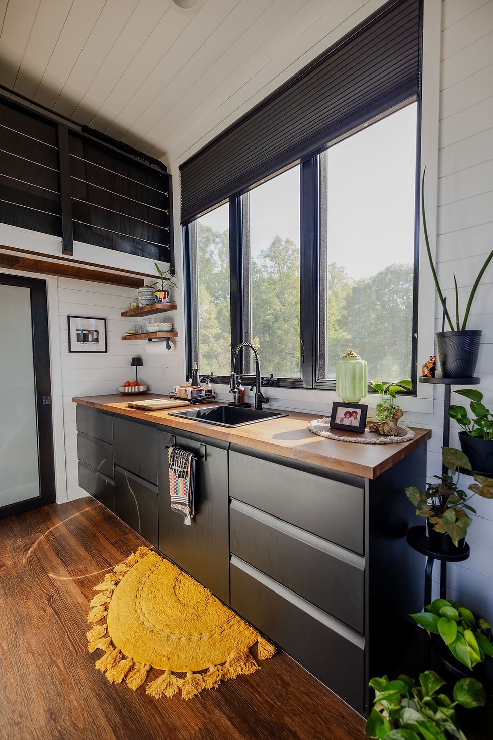 a tiny home kitchen with long counters and three tall windows above a deep sink
