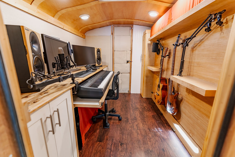 Soundproofed studio inside a school bus with a keyboard, monitors and a folding bed