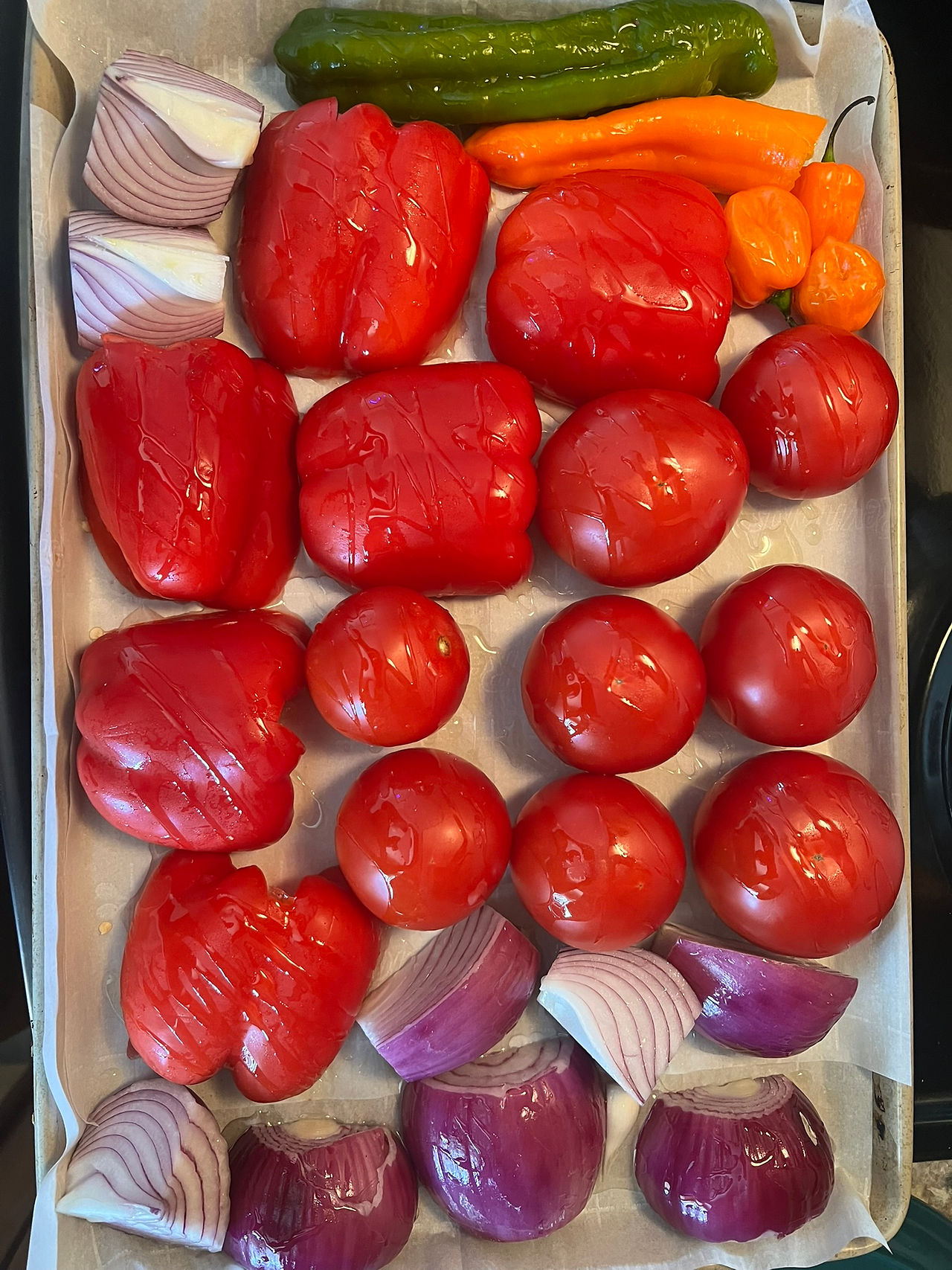 Tomatoes, red bell peppers, habaneros, red onion, and garlic arranged on a roasting tray.