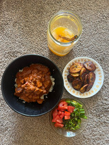 Plate of domoda with fried plantains and collard greens, paired with a glass of fresh orange juice. 