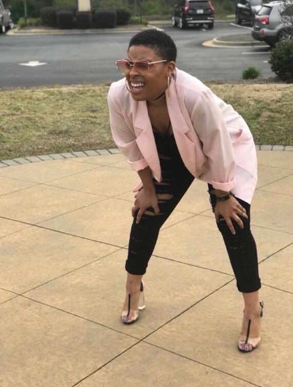 Black woman squinting meme - A Black woman wearing a pink blazer and ripped black jeans and heels with her hands on her knees squiting through sunglasses into the future. 