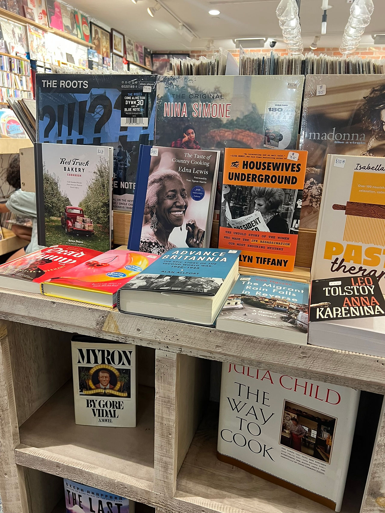 Bookstore table displaying cookbooks, history books, music biographies, and vinyl records, including works by Nina Simone and The Roots.