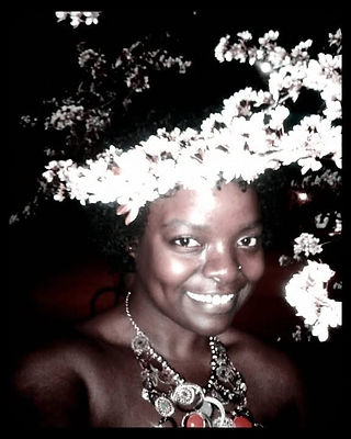 A nighttime portrait from 2011 showing the artist smiling beneath blooming white tree branches while wearing a large statement necklace and nose ring. The blossoms frame their face against a dark background.