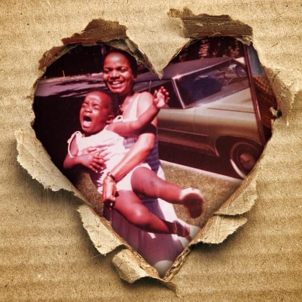 Vintage family photograph of a Black woman holding a crying child in front of a car, presented through a torn heart-shaped opening in textured paper.