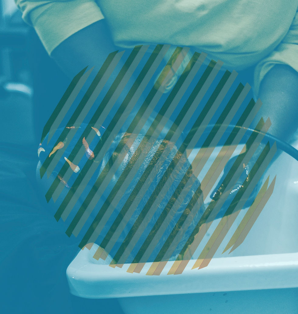A cyan-toned overhead image of a client’s wet hair resting inside a white shampoo bowl while a stylist’s hands work nearby. Dark diagonal bars cross the client’s head, partially obscuring the act of care.