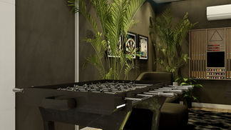 Sala de jogos residencial com mesas de sinuca e pebolim, sofá e painel com TV, integrada visualmente ao jardim de inverno por amplas aberturas envidraçadas. O ambiente apresenta piso e painéis amadeirados, iluminação direta sobre as mesas e vegetação interna, criando uma atmosfera acolhedora, elegante e conectada à natureza.