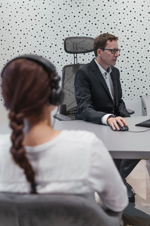 Mitarbeiter im Büro, ein Mann am Computer, eine Frau mit Kopfhörern