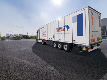 Weißer Schmitz-Cargobull-Sattelauflieger auf leerem Asphaltplatz im Sonnenlicht, mit blauen Logos und Stadt im Hintergrund.