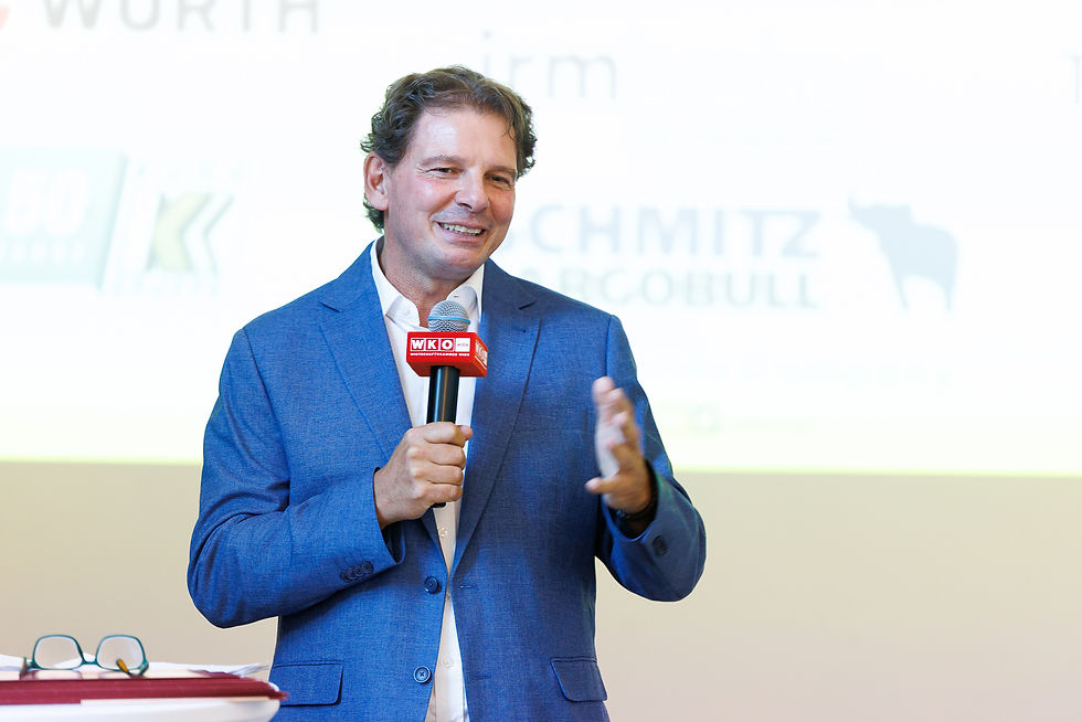 Mann im blauen Anzug spricht lächelnd ins WKO-Mikrofon vor hellem Hintergrund.