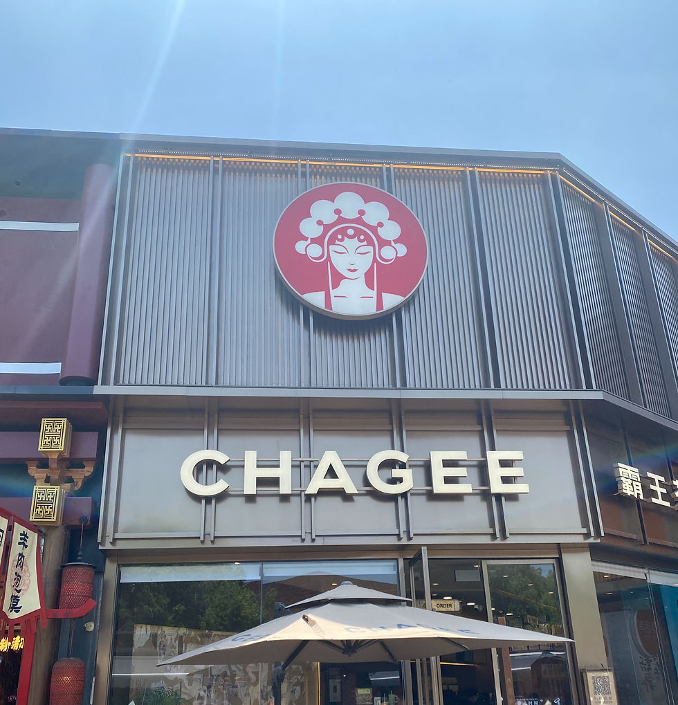 Facade view of a CHAGEE store with red logo, large lettering and parasol under a blue sky.