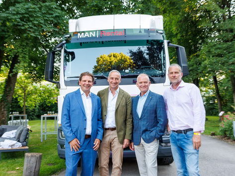 Vier Männer posieren lächelnd vor einem weißen MAN Rental-Lkw im grünen Park.