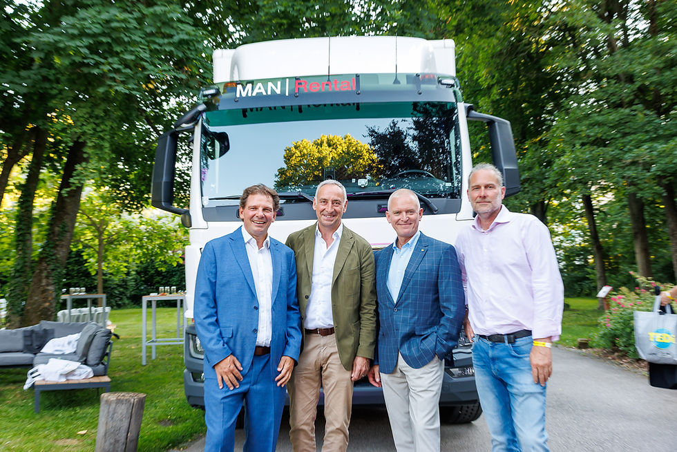Vier Männer posieren lächelnd vor einem weißen MAN Rental-Lkw im grünen Park.