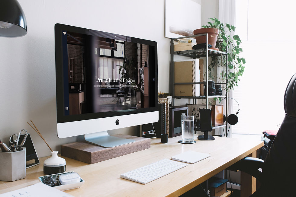 Moderner Schreibtisch mit iMac, der "Prime Interior Designs" Webdesign zeigt. Pflanzen und Bücher im Hintergrund sorgen für eine ruhige Atmosphäre.
