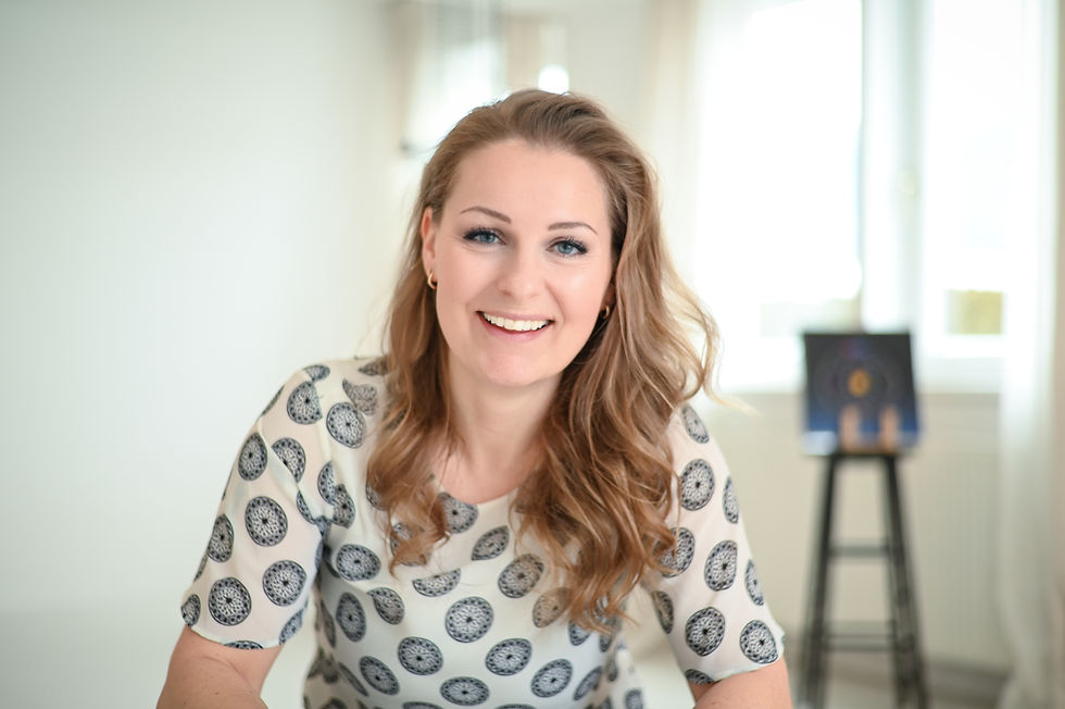 Smiling brand designer Helene Clara Gamper sits in a bright room wearing a patterned top. A painting on an easel stands in the background. A relaxed, friendly atmosphere.