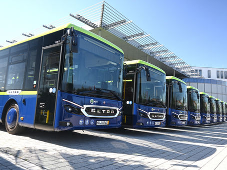 Reihe blauer Setra-Linienbusse mit grünem Rand vor modernem Gebäude; sonniger Himmel, vorne MVV-Logo und Kennzeichen.